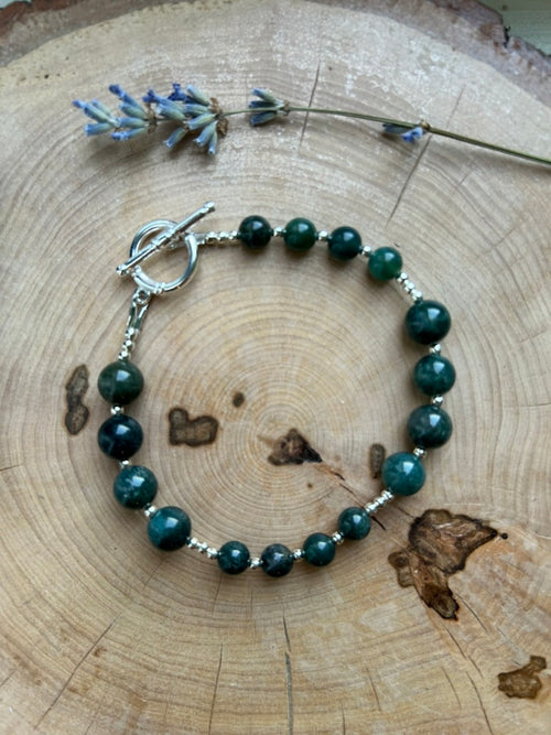Moss agate breathwork bracelet with 925 silver-plated toggle clasp on a wooden slice with lavender
